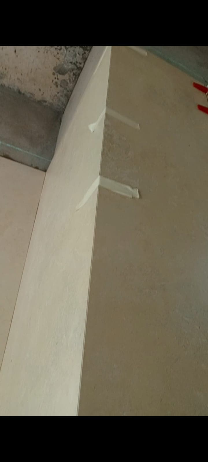 External corner of two large cream porcelain wall tiles held with masking tape while the adhesive cures, Askari 10 bathroom, Islamabad