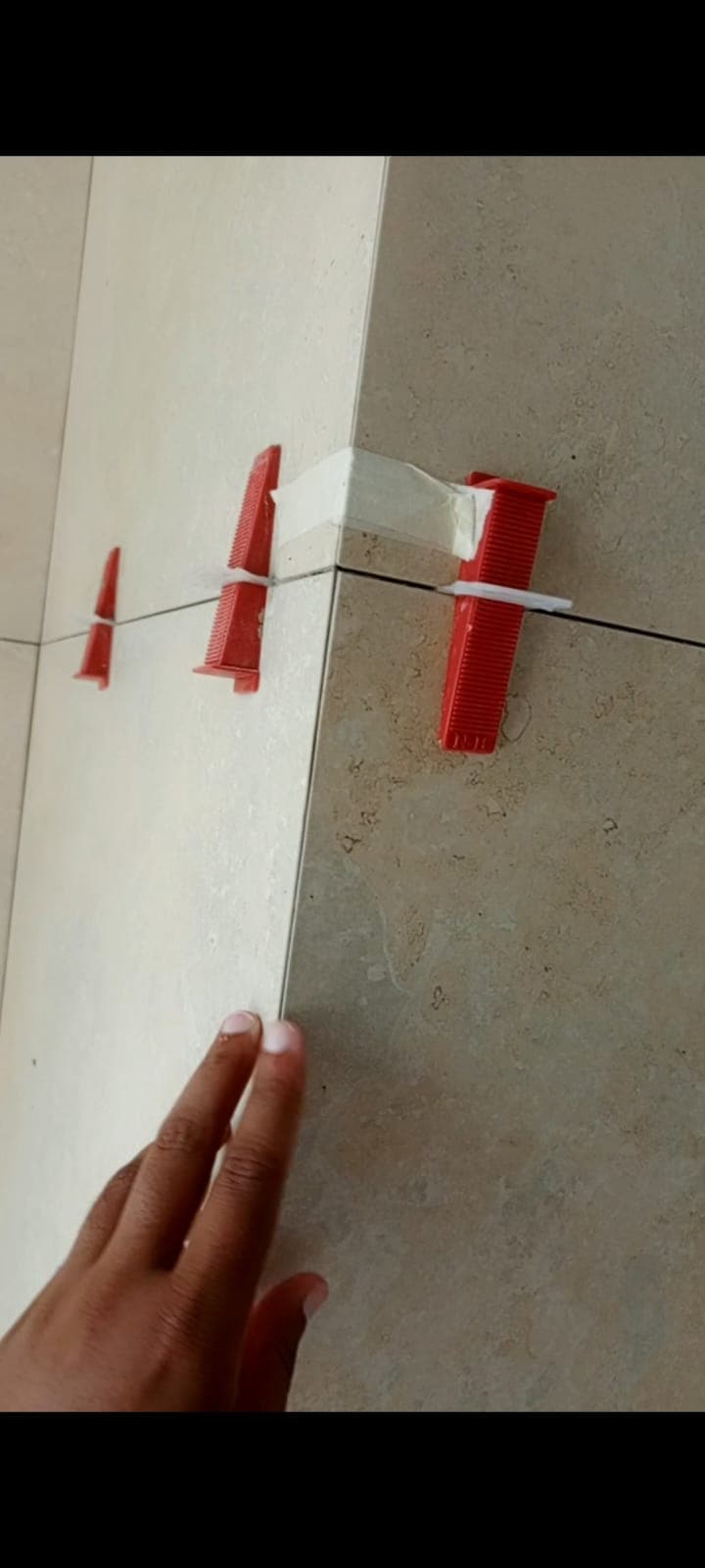 Red tile levelling clips and wedges holding a wall tile joint flush, Askari 10 bathroom, Islamabad