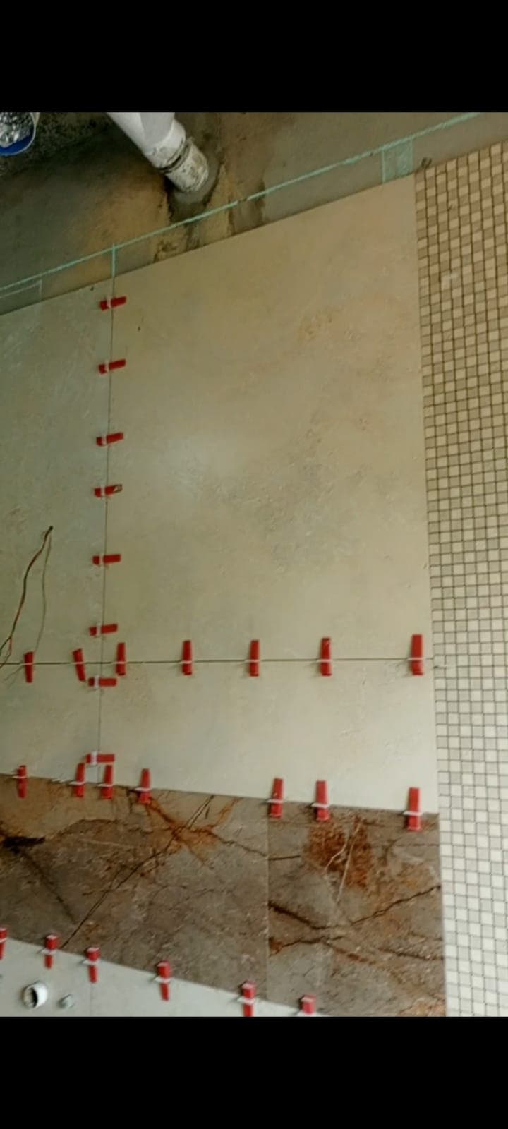 Bathroom wall corner where large cream porcelain tiles meet a brown feature band and a beige mosaic strip, Askari 10 Islamabad