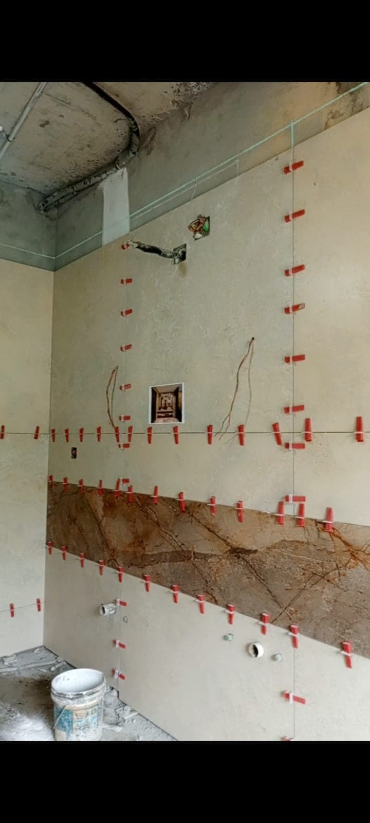 Master bathroom wall being tiled with large-format cream porcelain on levelling clips, with a brown vein-matched feature band, Askari 10 Islamabad