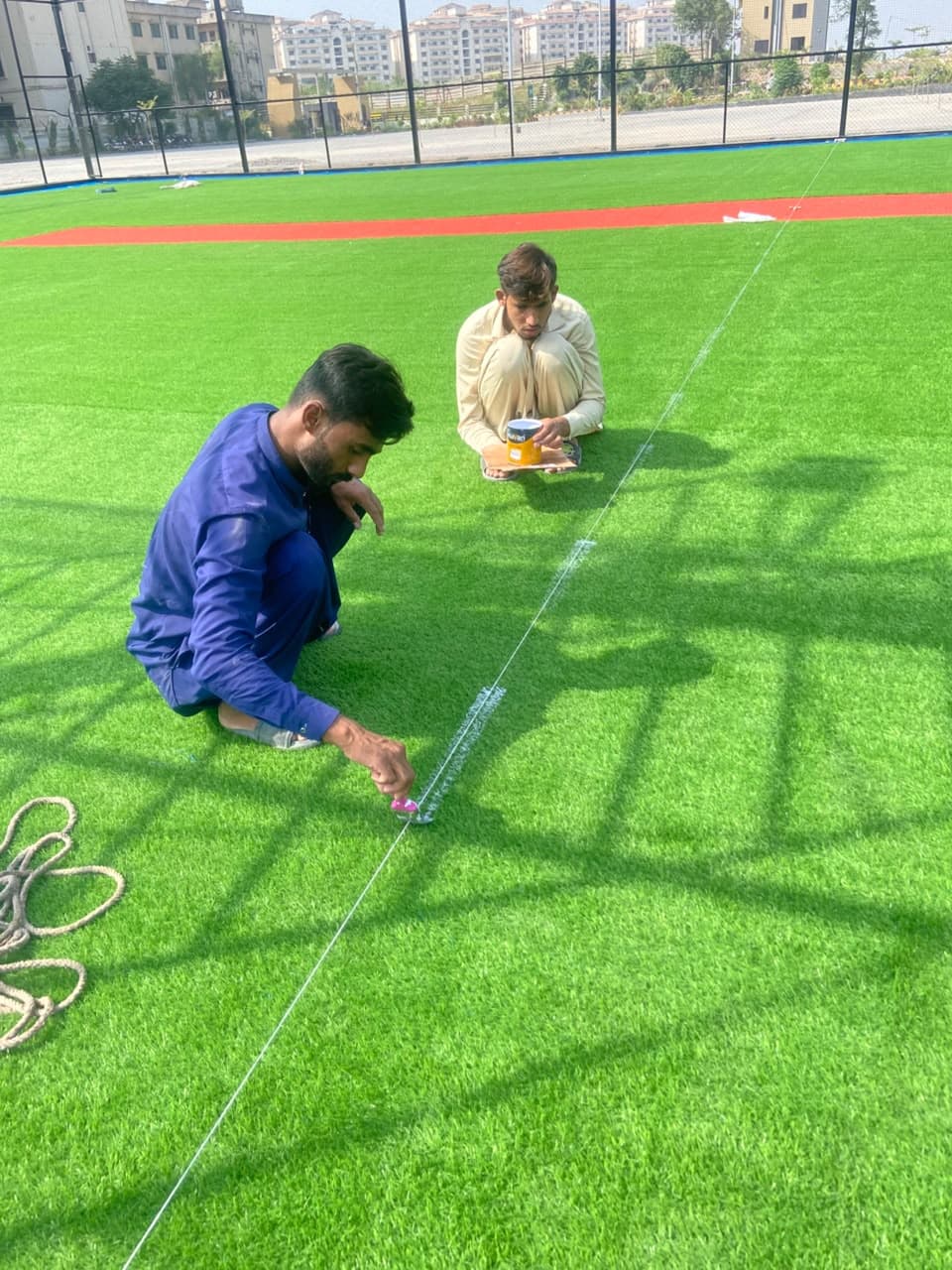 Installation technicians string-line marking boundary lines on green artificial turf at Football Ground Askari 14