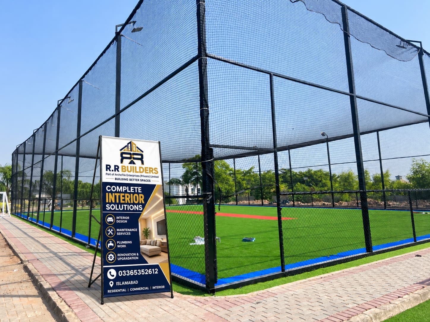 Entrance view of Football Ground Askari 14 featuring R.R Builders standee banner, sports fencing, and floodlights