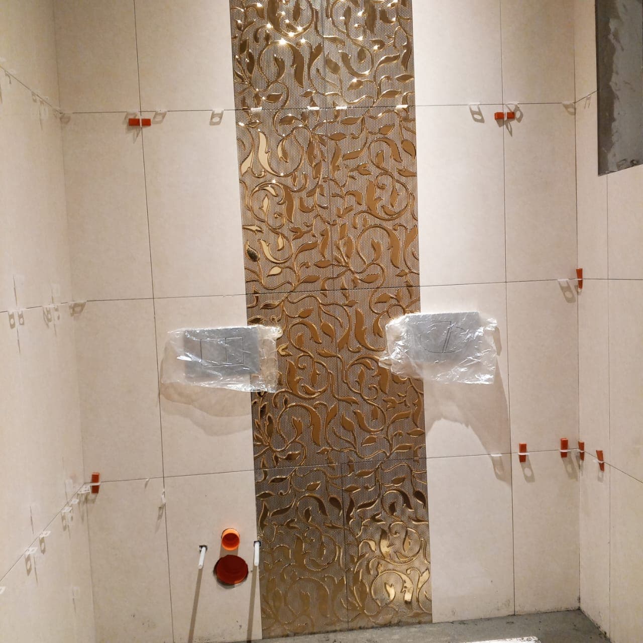 Bathroom wall tiling in progress featuring cream porcelain tiles and an ornate gold relief accent strip held with levelling clips in F-6 / F-7 Islamabad