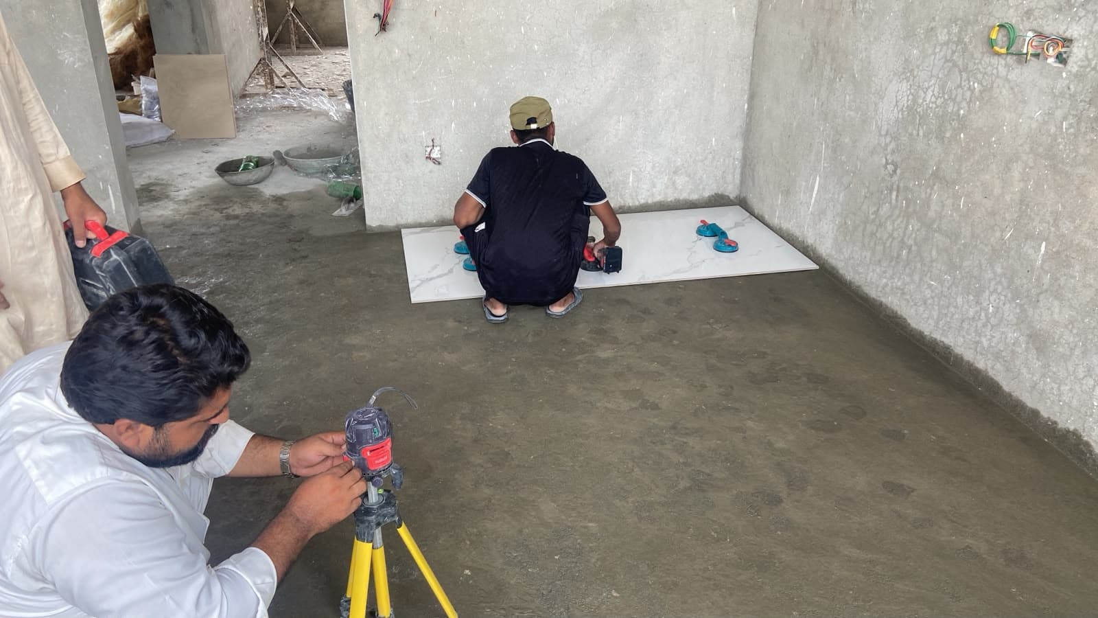 Large-format white marble-look porcelain floor tiles being laid with laser guidance in a 1 kanal house, Faisal Hills Islamabad