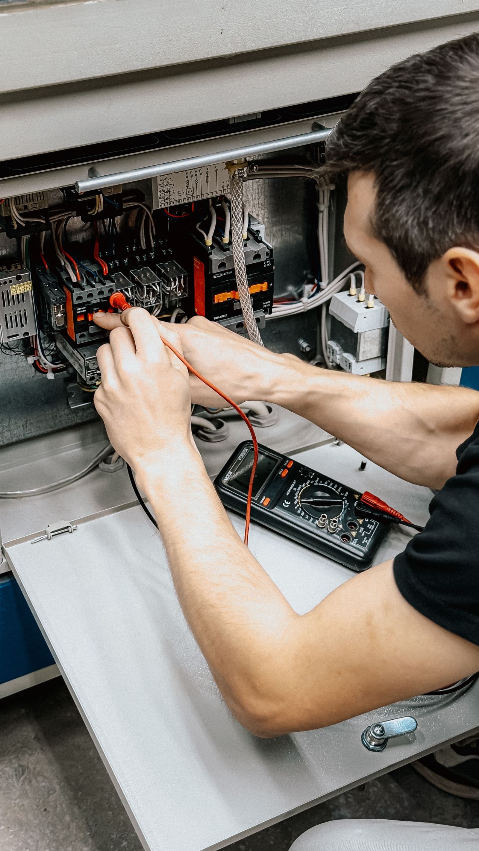 Electrician testing an open electrical panel with a multimeter
