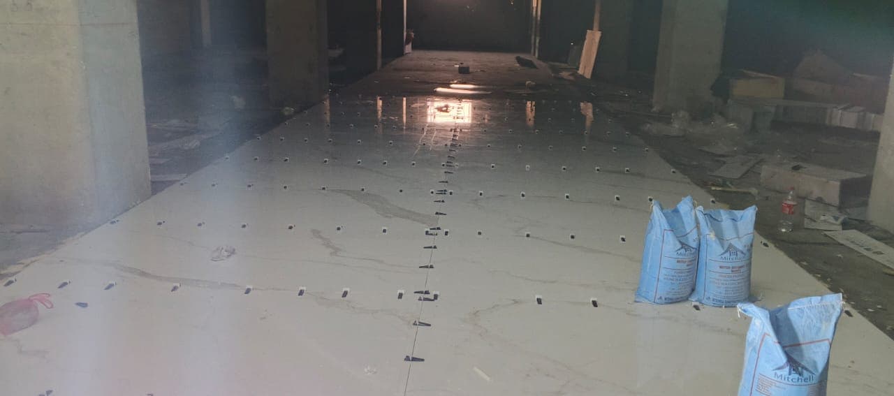 Large-format marble-look floor tiles being fixed with levelling clips in a G-14 Islamabad house